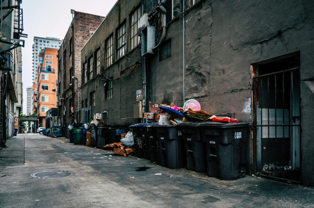 A gritty urban alley in Seattle with overflowing trash bins and high-rise buildings.